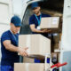 young courier his colleague unloading cardboard boxes from delivery van 80x80
